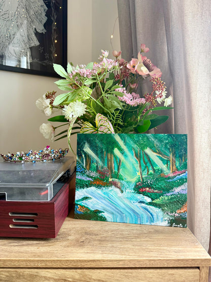 A small landscape painting of a forest stream with green trees, blue water, and sunbeams, displayed on a wooden cabinet next to a flower arrangement and a record player.
